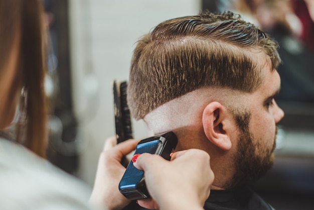 Beautiful girl hairdresser cuts a bearded man in the salon