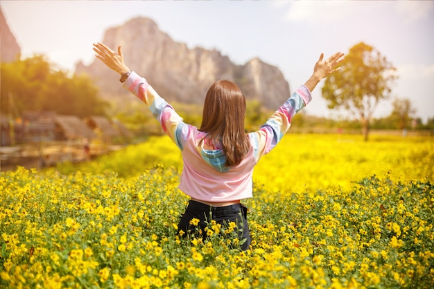 Beautiful girl hands up and looking far away in the yellow flower garden to relax and happy.