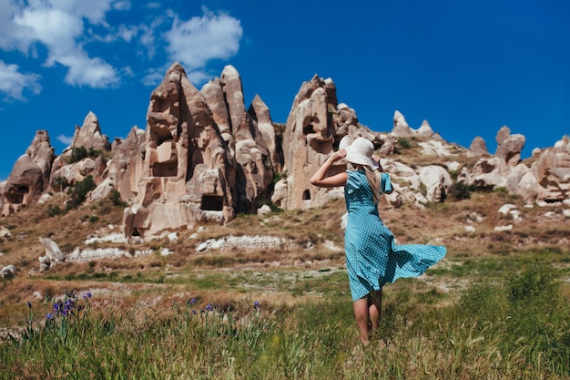 Beautiful girl in a hat and a turquoise dress looks at the mountains of Cappadocia