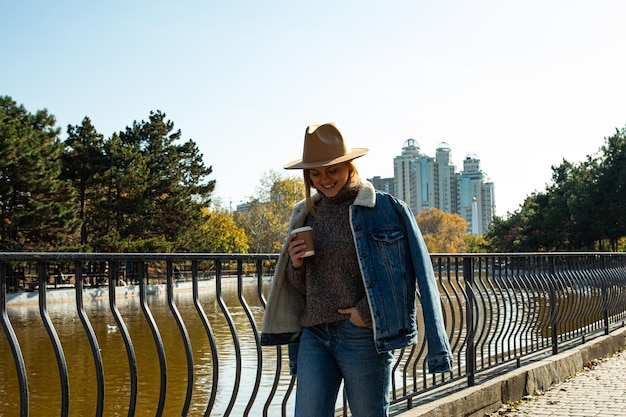 A beautiful girl in a hat walks in an autumn park with coffee