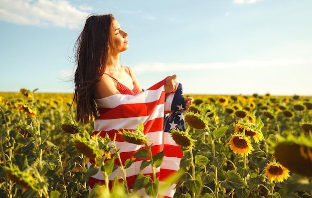 ひまわり畑にアメリカの国旗を掲げた帽子をかぶった美しい少女 独立記念日 7 月 4 日 自由