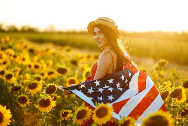 Beautiful girl in hat with American flag in a sunflower field 4th of July Independence Day