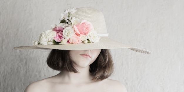 Beautiful girl in hat with flowers on gray background