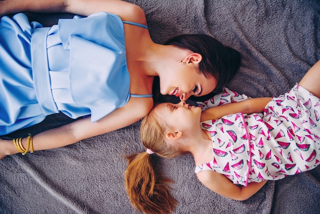 A beautiful girl and her young mother lying on a blanket and smiling to each other. Close up portrait of beautiful mom and her daughter.