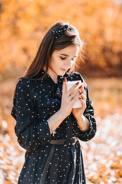 晴れた秋の日にコーヒーのグラスを保持している美しい少女