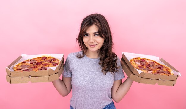 A beautiful girl holds in her hands two boxes of pizza on a pink background.