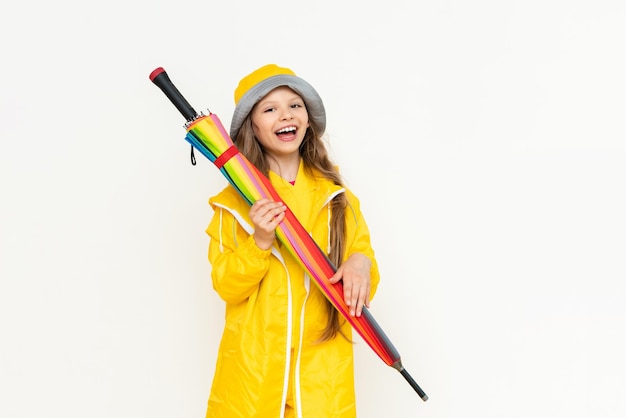 A beautiful girl holds a multicolored closed umbrella on a white isolated background A child dressed in a yellow raincoat and a panama hat from the rain Rainy weather concept