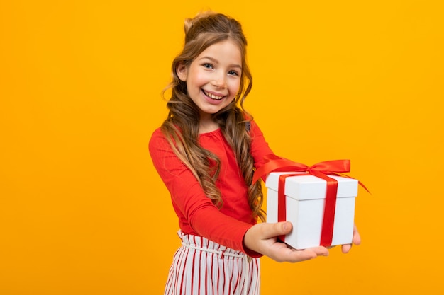 Beautiful girl holds out a box with a birthday present on yellow