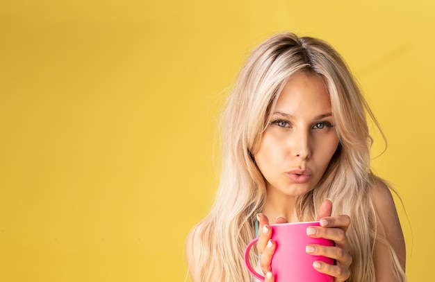 A beautiful girl holds a pink mug in her hands on a yellow background, in the studio