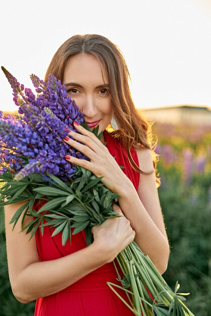 写真 赤いドレスを着た美しい女の子が ⁇ 野にルピンの花を ⁇ かせています ⁇