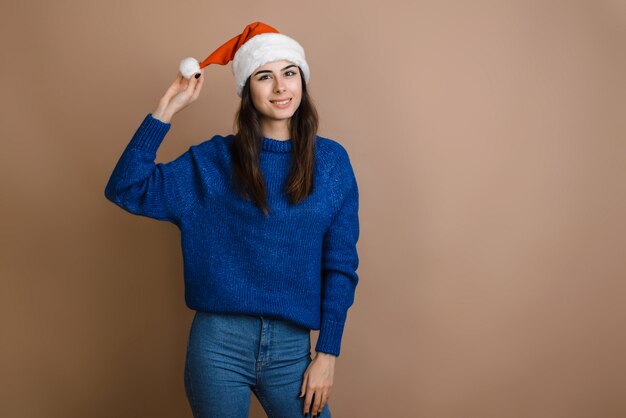 写真 幸せと興奮を探している茶色の背景に赤いサンタクロースの帽子で美しい少女。幸せなクリスマスと新年の休暇。