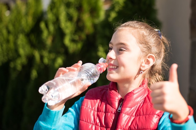 Красивая девушка пьет воду под жарким солнцем в парке Здоровая концепция Концепция здорового образа жизни