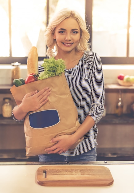 Beautiful girl is holding a paper shopping bag with food.