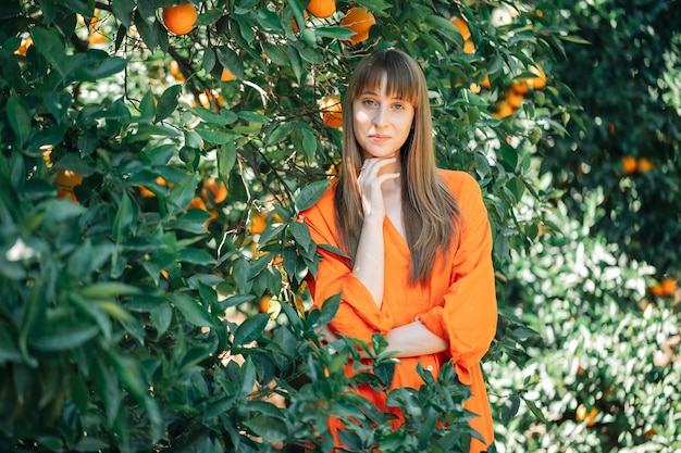 Beautiful girl is posing to camera by holding hand under chin in orange garden