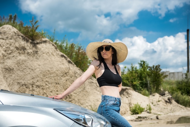 Bella ragazza sta riposando fuori città e posa vicino all'auto