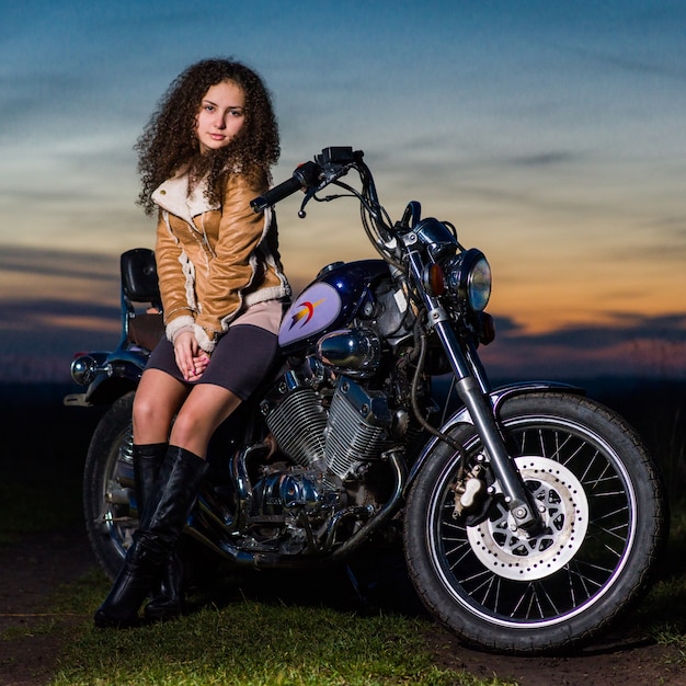 Beautiful girl is sitting on a motorcycle in the evening