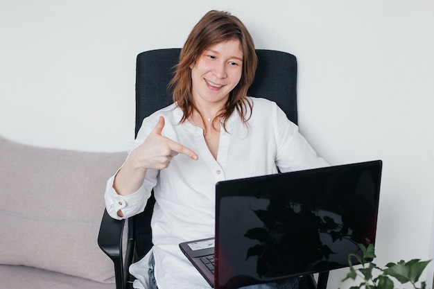 The beautiful girl is sitting in an office chair at home with a laptop in her hands, with positive emotions and a beautiful smile