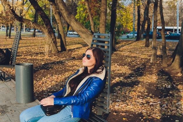 A beautiful girl is sitting on a park bench on a background of green nature.