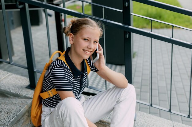 Foto una bella ragazza è seduta sulle scale della scuola tra le lezioni e parla al telefono