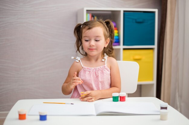 A beautiful girl is sitting at a table and learning to draw with a paint brush