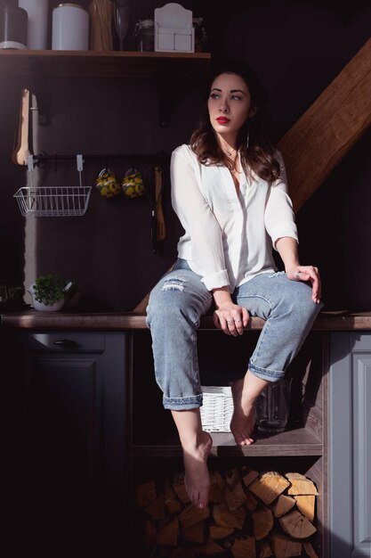 Beautiful girl in jeans and a white shirt poses in the kitchen in the rays of sunlight sensual woman