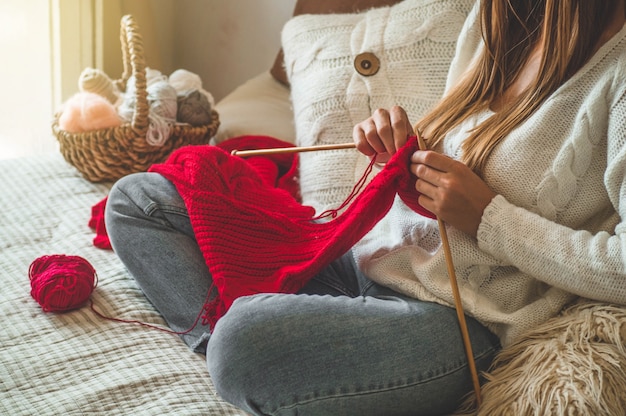 写真 美しい少女はベッドに暖かいセーターを編んでいます。趣味の編み物。編み物用アクセサリー。