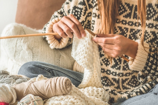 Beautiful girl knits a warm sweater on the bed. Knitting as a hobby. Accessories for knitting.