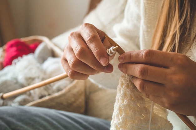 Beautiful girl knits a warm sweater on the bed. Knitting as a hobby. Accessories for knitting.