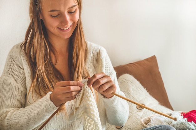 Beautiful girl knits a warm sweater on the bed. Knitting as a hobby. Accessories for knitting.