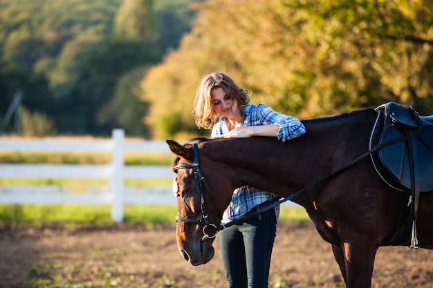 Beautiful girl leading her brown horse at the farm