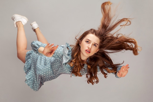 Beautiful girl levitating in mid-air, falling down and her hair messed up soaring from wind