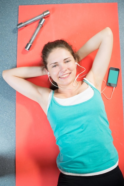 Photo beautiful girl lies and rests after training on the mat in the gym