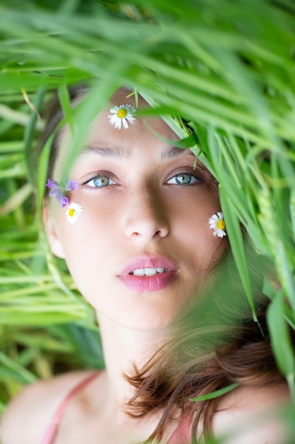 Foto bella ragazza si trova con gli occhi chiusi sul campo di grano verde con fiori selvatici sul viso