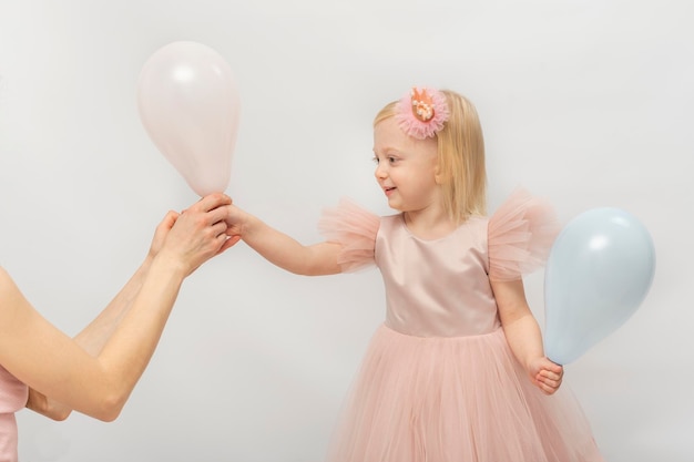 Beautiful girl in lush pink dress smiling takes balloon from hands of woman Little blonde princess isolated on white background