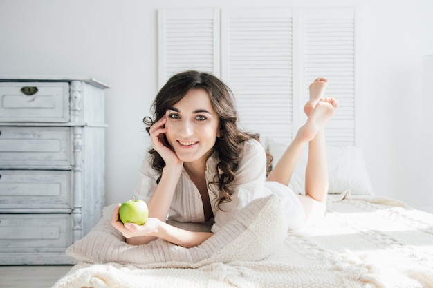 Beautiful girl lying in bed and holding an Apple