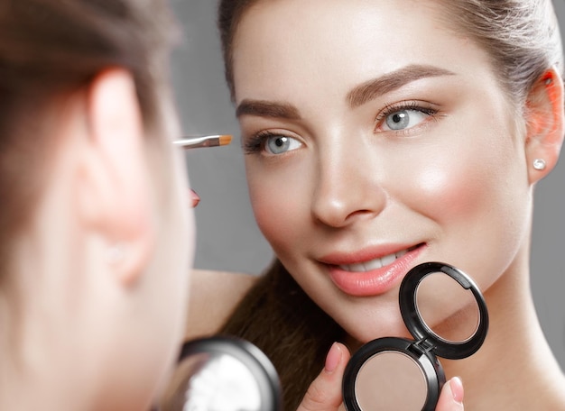 Beautiful girl makes herself a makeup in the mirror Beauty face Photo taken in studio