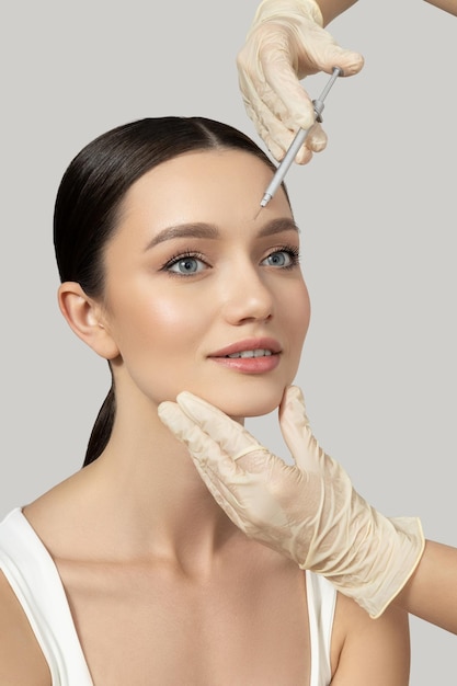 A beautiful girl makes an injection of botox on a gray background