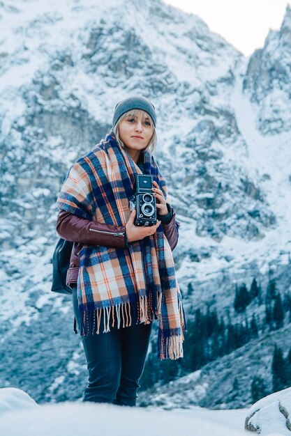 Beautiful girl makes a photo on an old vintage camera on a background of snowcapped mountains