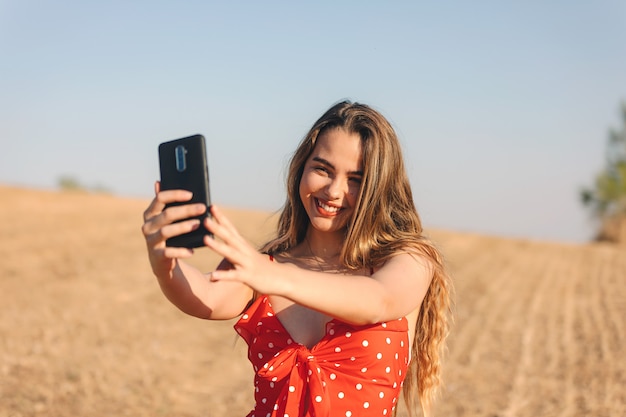 Beautiful girl makes a selfie outdoors in a summer sunset