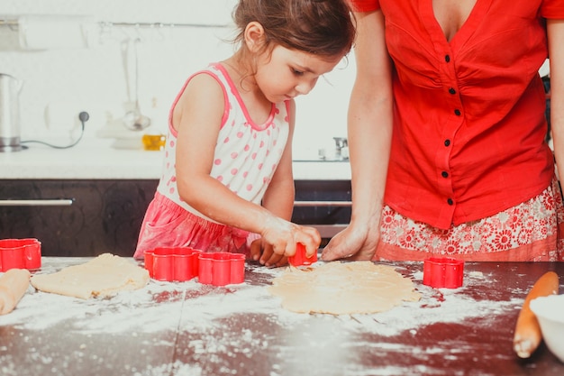 The beautiful girl makes shapes of dough in the form of a flower, and mom next to her in the kitchen