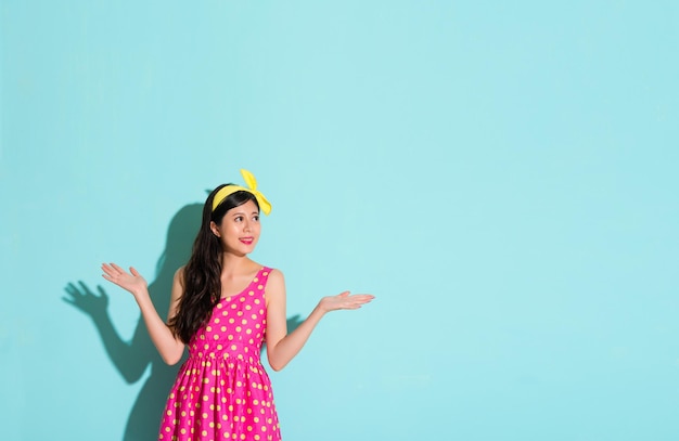 beautiful girl making a gesture of choice and looking at the blue copyspace of the advertising content smiling standing on the blank area showing cute color dress skirt clothing.