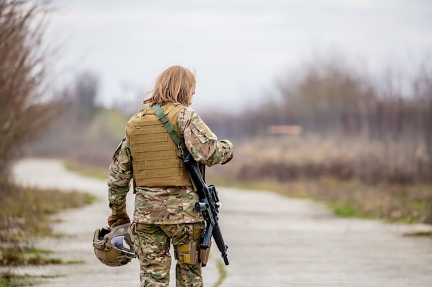Красивая девушка в военной форме с пистолетом для страйкбола гуляет по дороге