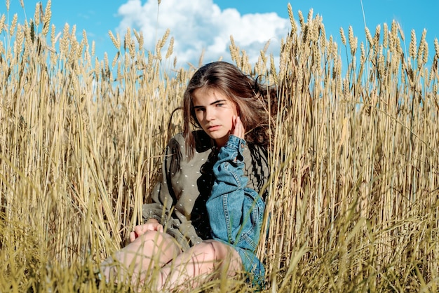 Beautiful girl model in dress in the countryside. Against the background of a field among wheat. Blue sky, Freedom and hot summer concept.