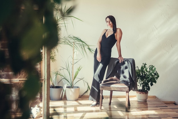 Beautiful girl model dressed in black clothes standing near armchair in loft style interior