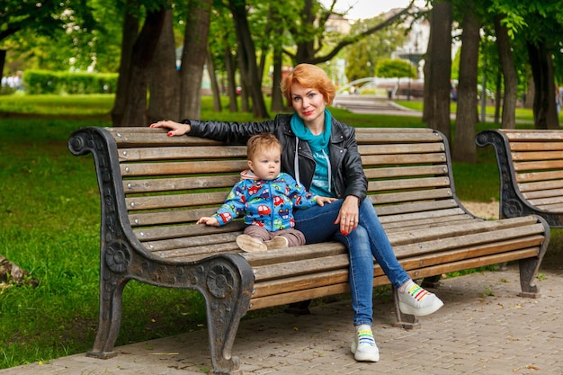 Красивая девочка-мать с мальчиком-сыном в парке в парке сидят на скамейке