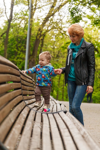 公園の公園で男の子の息子を持つ美しい少女の母親がベンチに座っています。