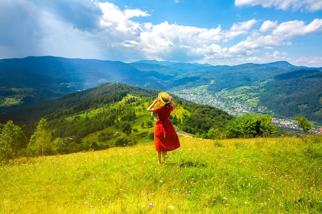 山の美しい少女。旅行中のリネンのドレスと麦わら帽子の女性。周りの素晴らしい夏の自然。調和と放浪癖の概念。素朴なナチュラルスタイル。ダイナミックな写真のための風が吹いています。