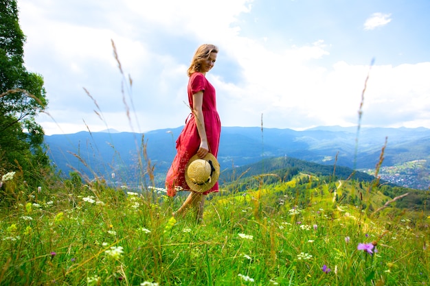 Photo beautiful girl the mountains. woman in linen dress and straw hat travelling. amazing summer nature around. harmony and wanderlust concept. rustic natural style. wind blowing for dynamic photo.