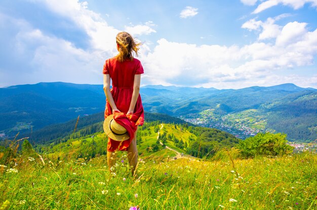 山の美しい少女。旅行中のリネンのドレスと麦わら帽子の女性。周りの素晴らしい夏の自然。調和と放浪癖の概念。素朴なナチュラルスタイル。ダイナミックな写真のための風が吹いています。