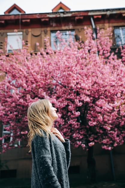 Foto bella ragazza vicino agli alberi di sakura donna in abito e cappotto elegante fiori rosa che sbocciano a uzhhorod blossom intorno al periodo primaverile concetto di relax e felicità